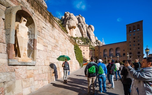 Tourists exploring Montserrat Sanctuary with stone carvings and mountain backdrop.