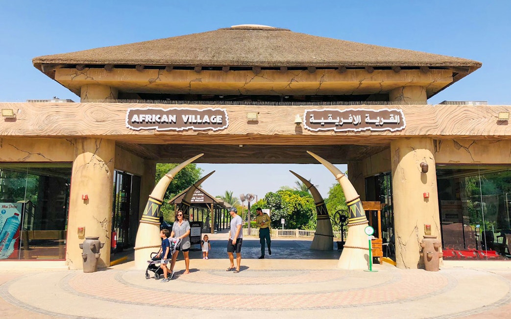 Entrance to African Village at Dubai Safari Park with visitors walking through.