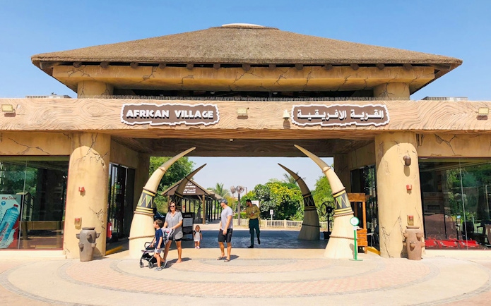 Entrance to African Village at Dubai Safari Park with visitors walking through.