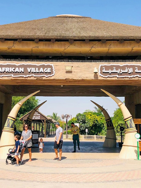 Entrance to African Village at Dubai Safari Park with visitors walking through.