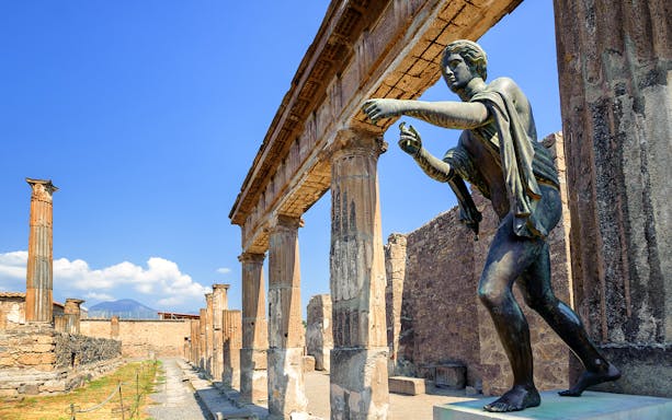 Ancient statue and columns at Pompeii with Mount Vesuvius in the background.
