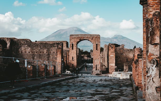 Ancient stone street leading to archway in Pompeii with Mount Vesuvius in the background.
