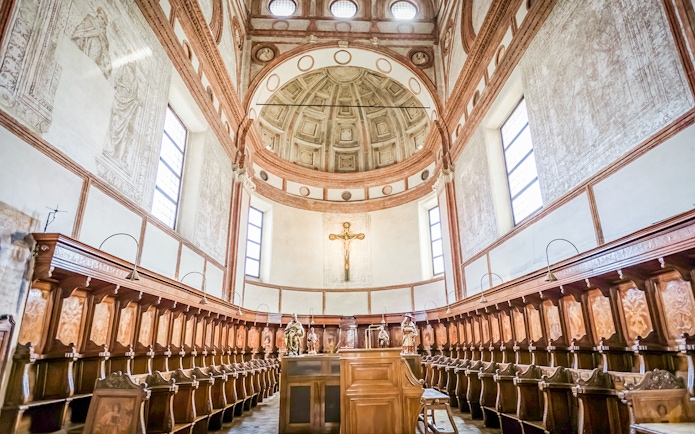 Interior of Santa Maria Delle Grazie Church with wooden choir stalls and a crucifix.