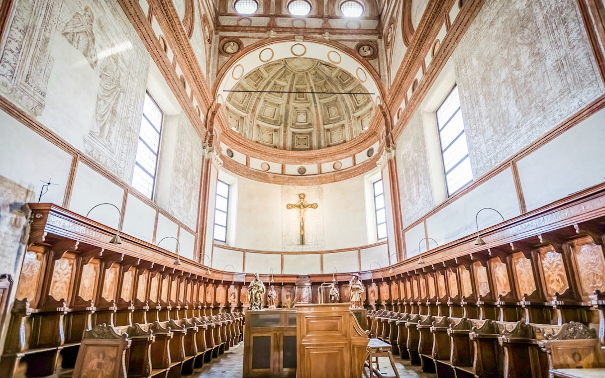 Interior of Santa Maria Delle Grazie Church with wooden choir stalls and a crucifix.