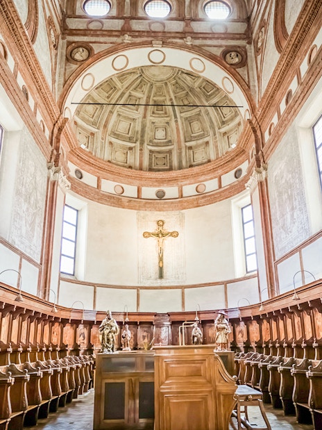 Interior of Santa Maria Delle Grazie Church with wooden choir stalls and a crucifix.