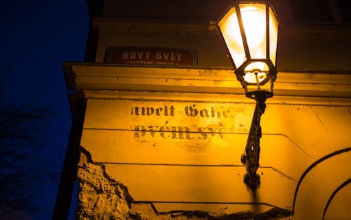Street lamp illuminating a wall with faded text in Nový Svět, Prague.
