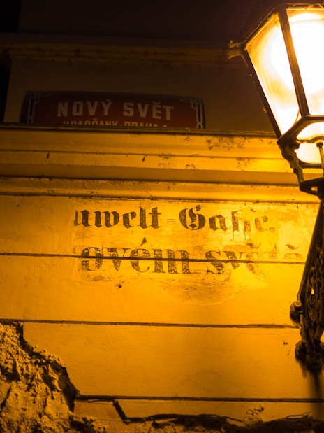 Street lamp illuminating a wall with faded text in Nový Svět, Prague.