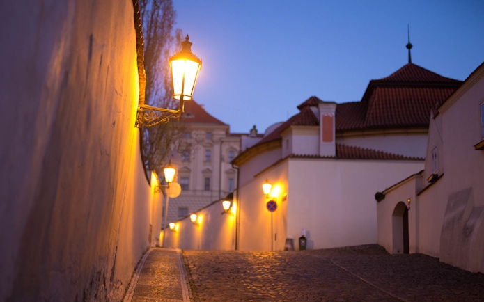 Cobblestone street with lanterns at dusk near Prague Castle.