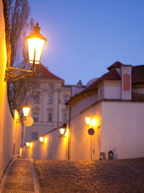 Cobblestone street with lanterns at dusk near Prague Castle.