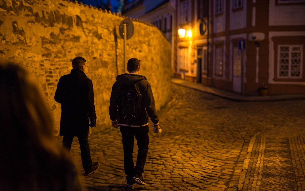 Visitors walking through cobblestone streets near Prague Castle at night.