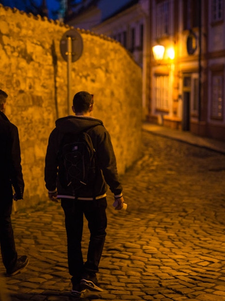 Visitors walking through cobblestone streets near Prague Castle at night.