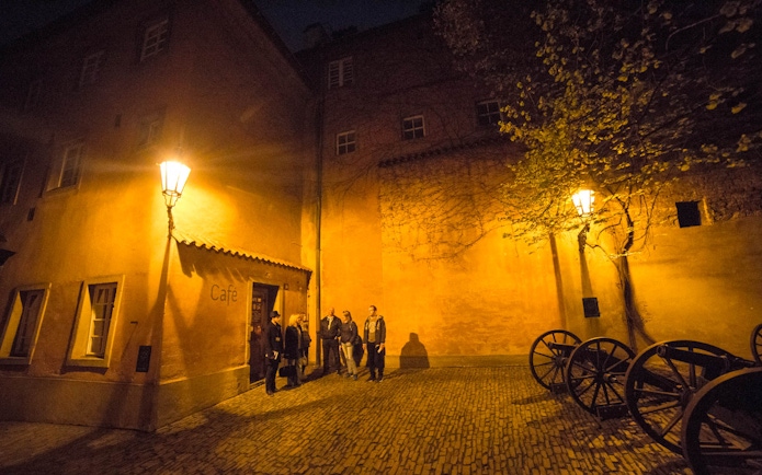 Visitors exploring a dimly lit courtyard near Prague Castle at night.