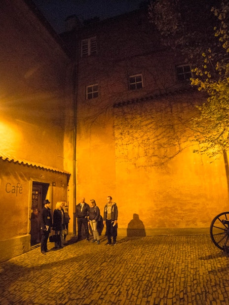 Visitors exploring a dimly lit courtyard near Prague Castle at night.
