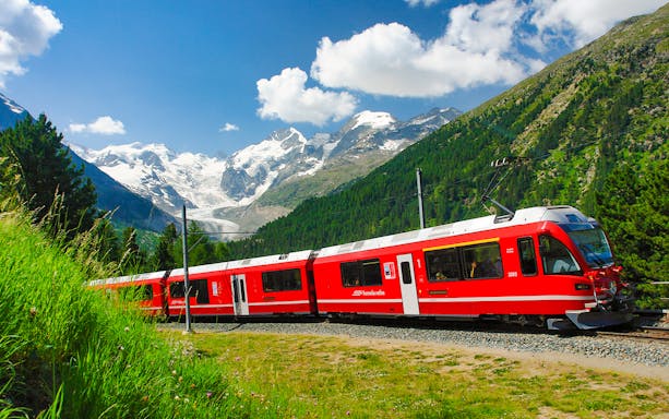Bernina Express train traveling through Swiss Alps with snow-capped mountains in the background.