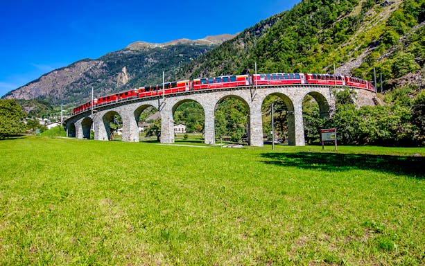 Bernina Express crossing a stone viaduct in the Swiss Alps on a day trip from Milan.