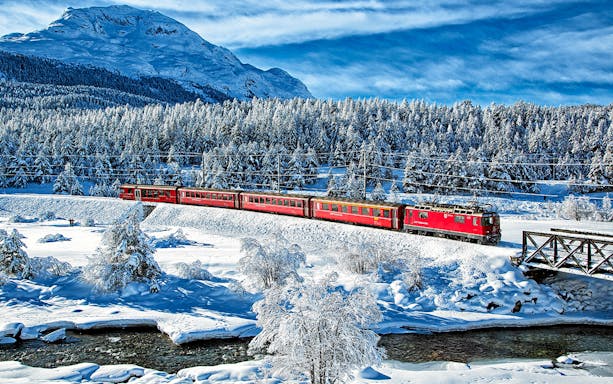 Bernina Express train traveling through snowy Swiss Alps landscape.