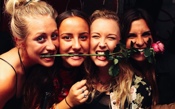 Group enjoying Prague pub crawl with rose in mouth.
