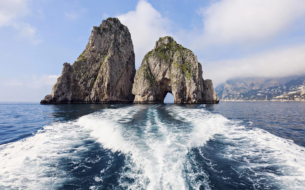 Boat approaching Faraglioni rock formations on Capri, Italy during a day trip from Naples.