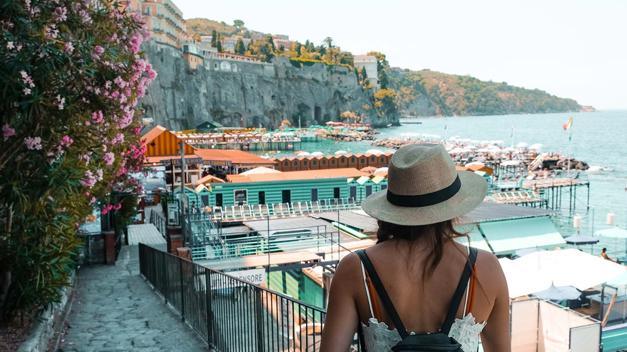 Tourist overlooking Sorrento coastline with colorful beach huts and cliffs.