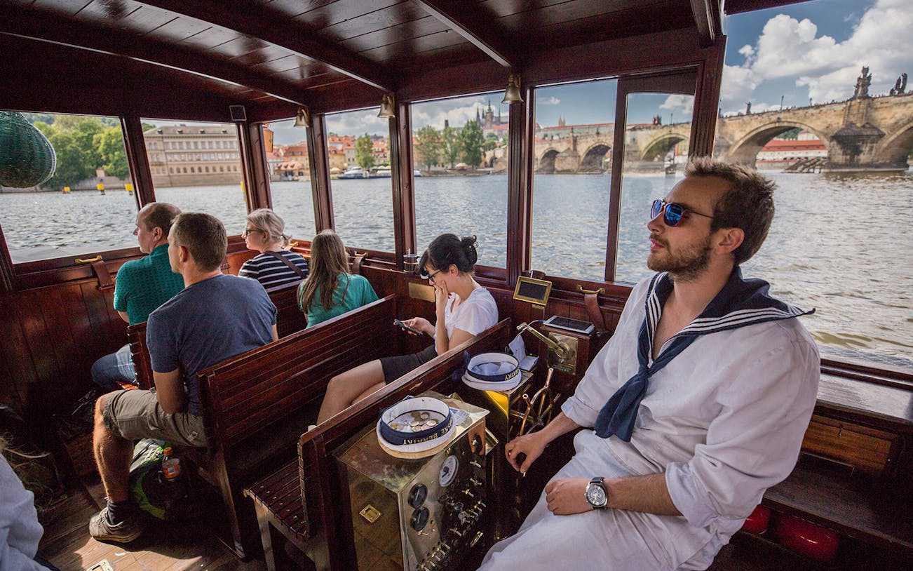 Tourists on a canal cruise boat with views of Charles Bridge and Prague Castle in Prague.