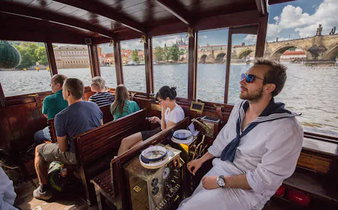 Tourists on a canal cruise boat with views of Charles Bridge and Prague Castle in Prague.