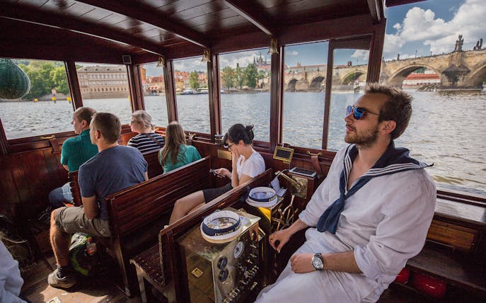 Tourists on a canal cruise boat with views of Charles Bridge and Prague Castle in Prague.