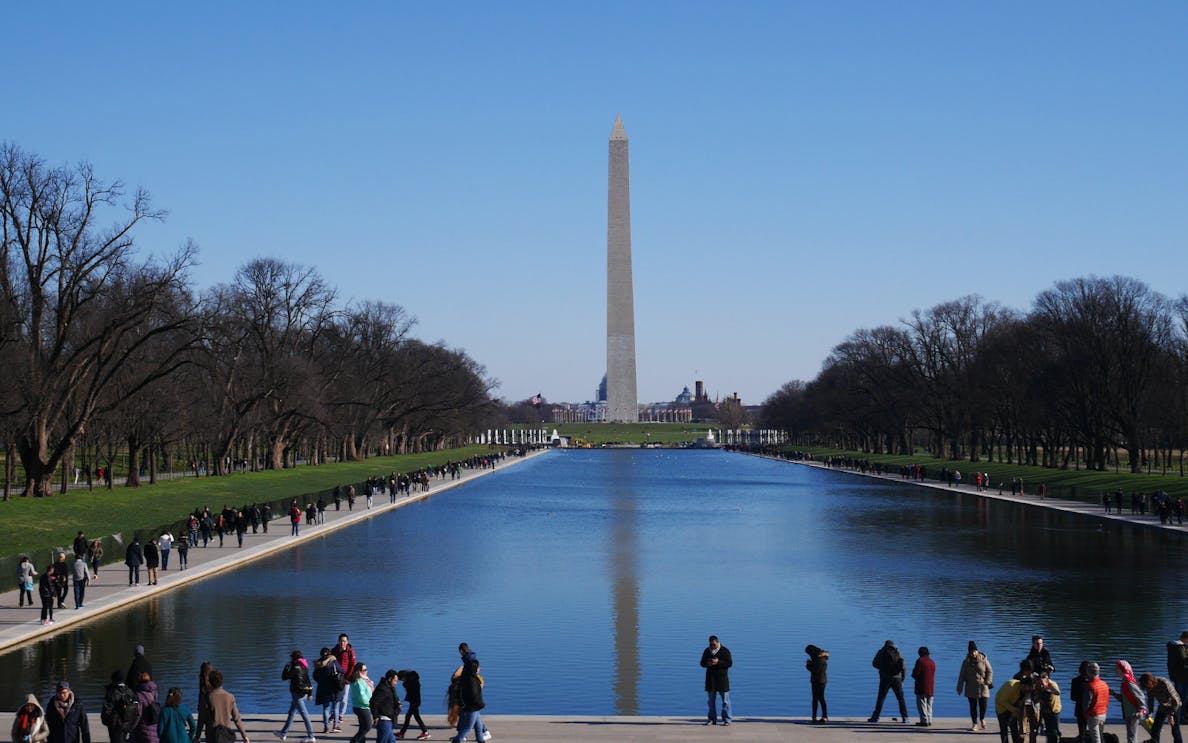 Reflecting Pool and Washington Monument in Washington, D.C., with visitors walking nearby.