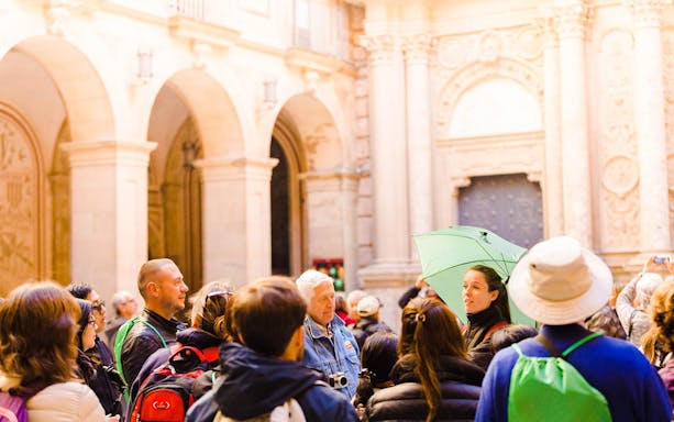 Tour group at Montserrat monastery courtyard with guide holding green umbrella.
