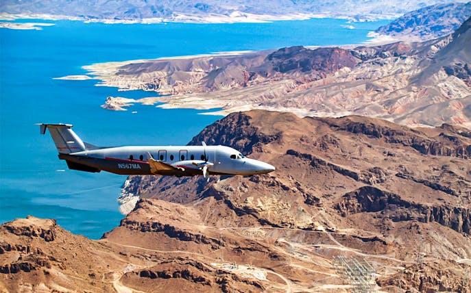 Airplane flying over Grand Canyon West Rim with view of rugged landscape and blue water.