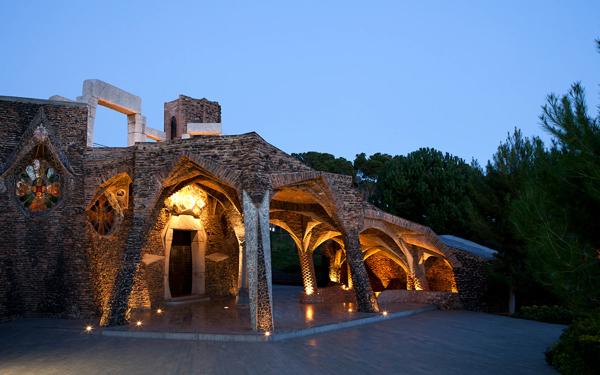 Colonia Güell Crypt illuminated at dusk, showcasing Gaudí's architectural design.