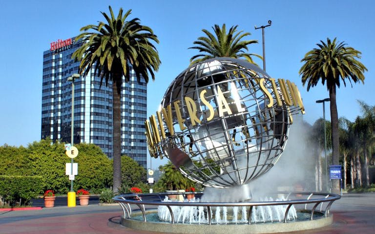 Universal Studios Hollywood globe sculpture with palm trees and hotel in background.