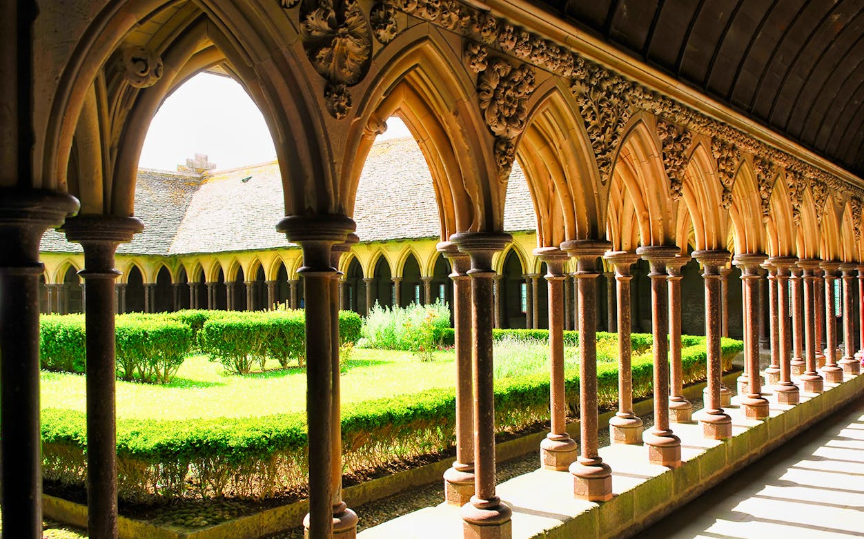Cloister arches at Mont St. Michel Abbey, France, with garden view.