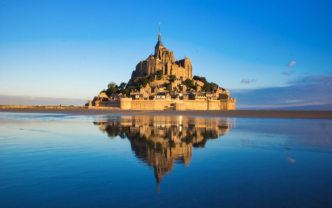 Mont St. Michel Abbey reflected in water during a full day tour from Paris.