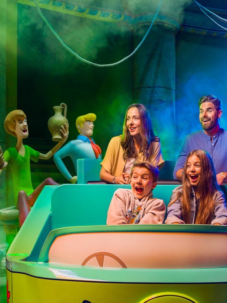 Visitors on a Scooby-Doo ride at Warner Bros. World™ Abu Dhabi, surrounded by animated characters.