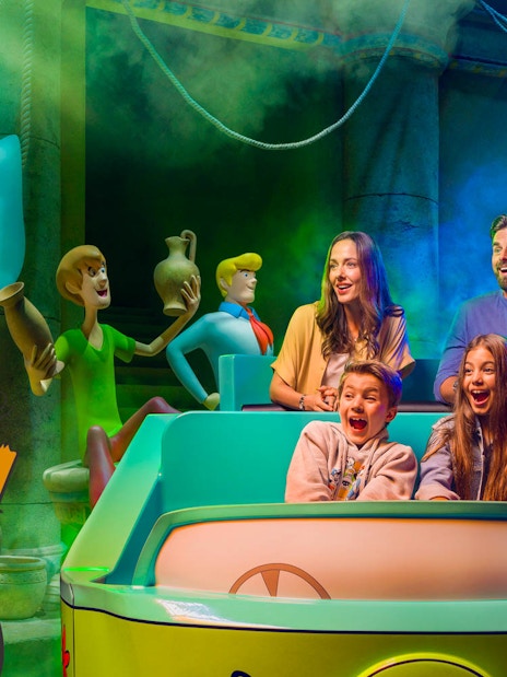 Visitors on a Scooby-Doo ride at Warner Bros. World™ Abu Dhabi, surrounded by animated characters.