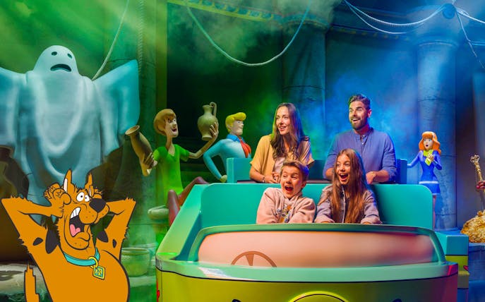 Visitors on a Scooby-Doo ride at Warner Bros. World™ Abu Dhabi, surrounded by animated characters.