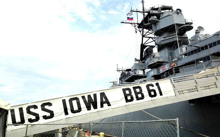 USS Iowa battleship docked in Los Angeles with gangway and flags visible.