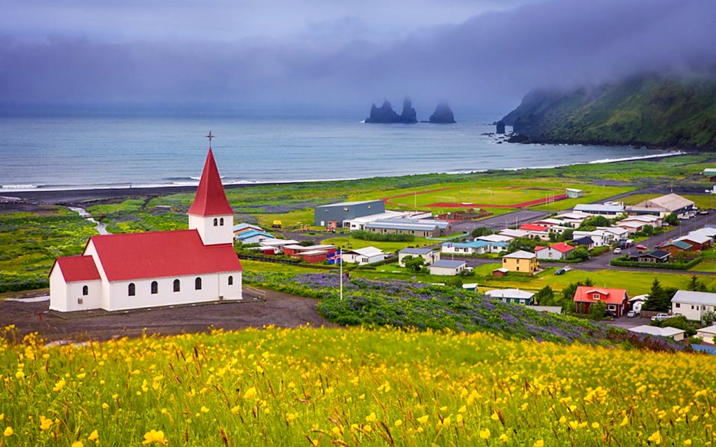 Church with red roof overlooking Vik village and Reynisdrangar sea stacks, Iceland.