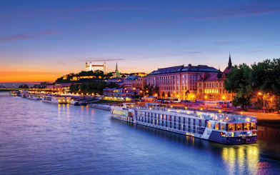 Late evening view of a river cruise ship docked near illuminated buildings in Bratislava.