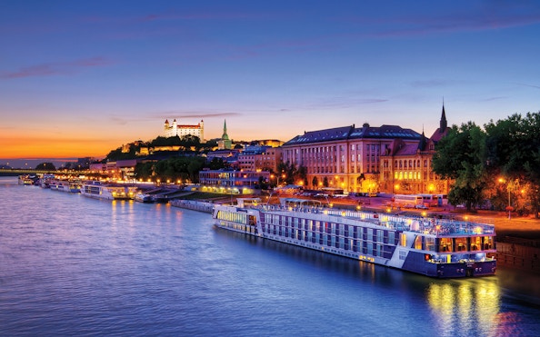 Late evening view of a river cruise ship docked near illuminated buildings in Bratislava.