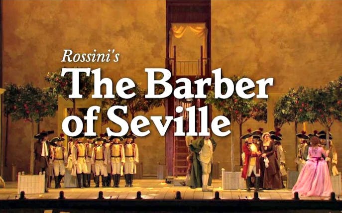 Opera performance of Rossini's The Barber of Seville with cast in period costumes on stage.