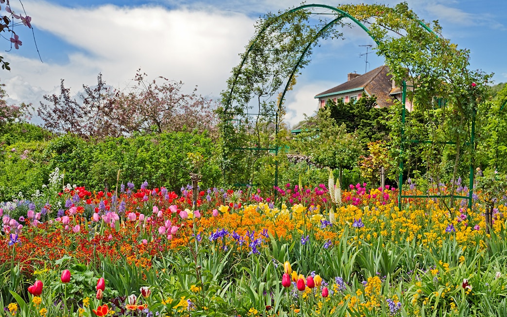 Colorful flower garden at Giverny with archway and house in the background.