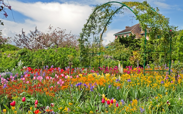 Colorful flower garden at Giverny with archway and house in the background.