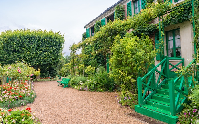 Giverny garden path with vibrant flowers and green shutters on a house.