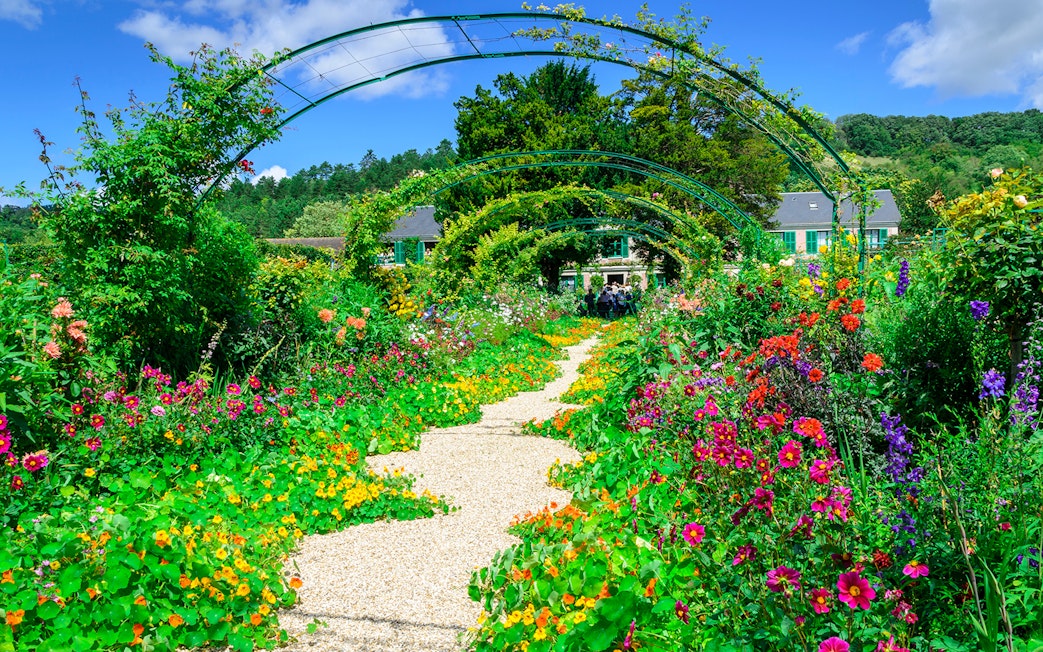 Pathway through vibrant gardens at Giverny, leading to Monet's house, part of Versailles & Giverny tour.