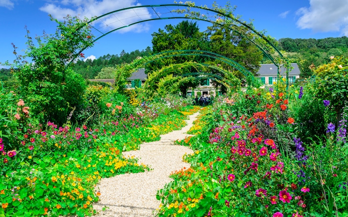 Pathway through vibrant gardens at Giverny, leading to Monet's house, part of Versailles & Giverny tour.