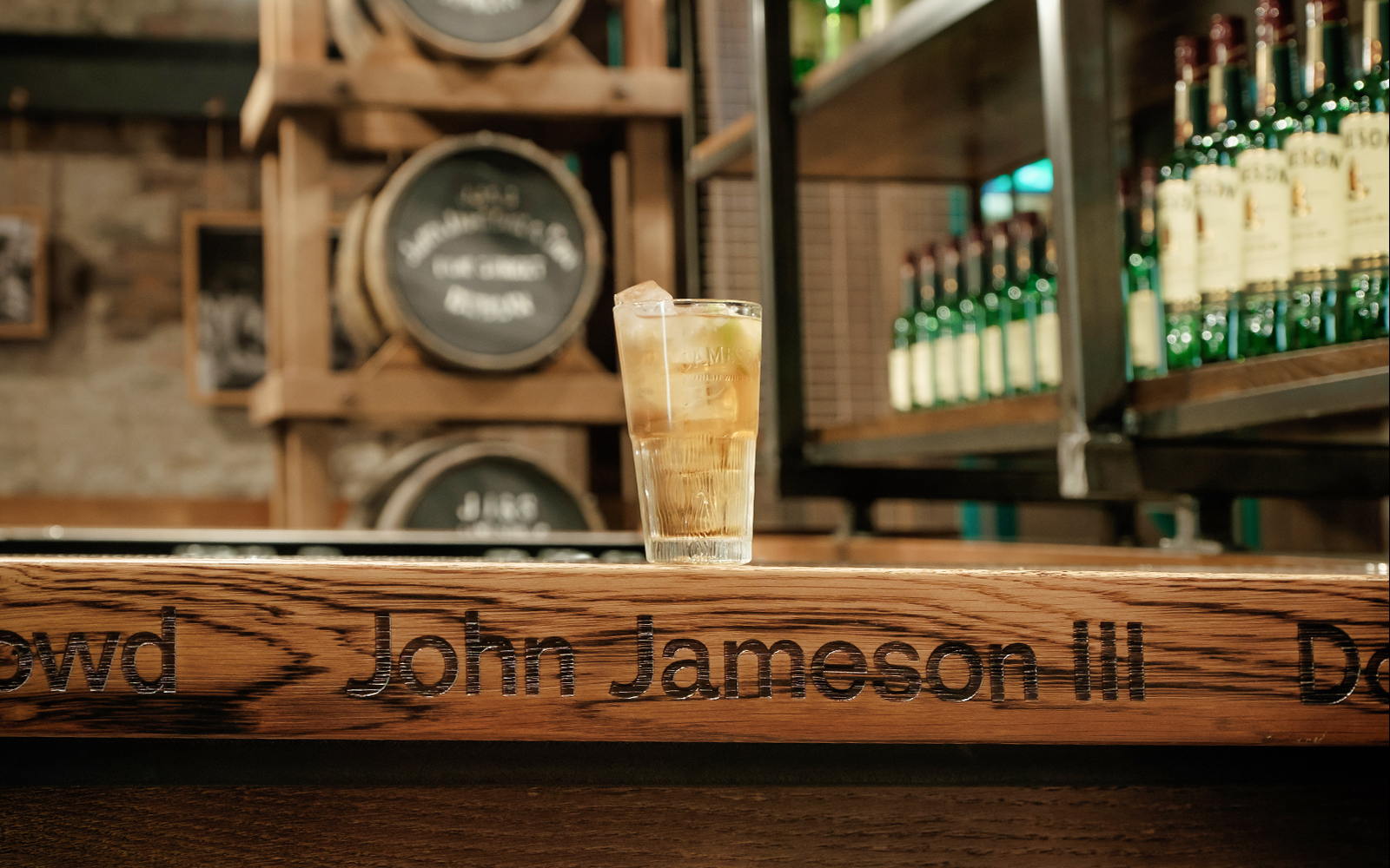 Glass of whiskey on a bar at Jameson Distillery, Dublin, with barrels in the background.