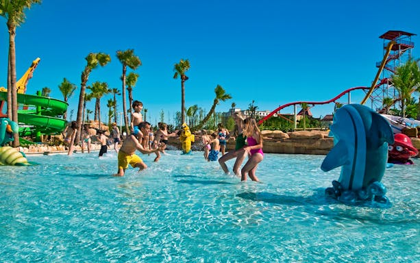 Children playing in a water park at PortAventura World with slides and palm trees.