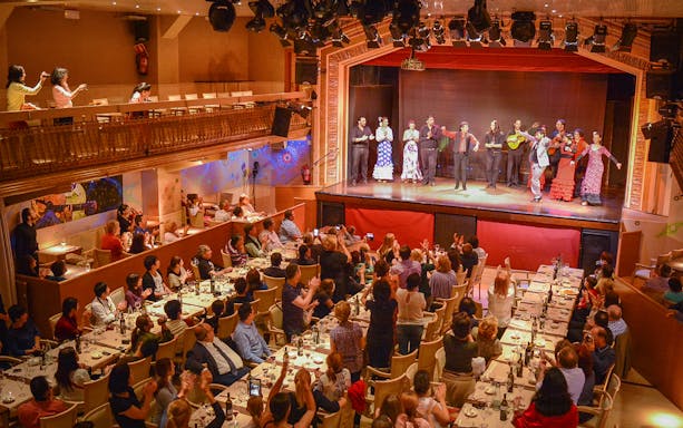 Flamenco dancers performing on stage with audience enjoying drinks in a lively venue.