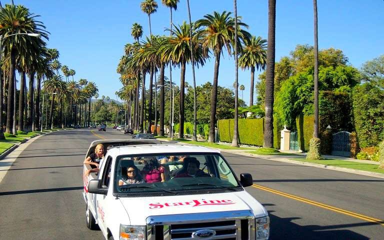 Tour van driving through palm-lined street on Movie Stars' Homes Tour in Los Angeles.